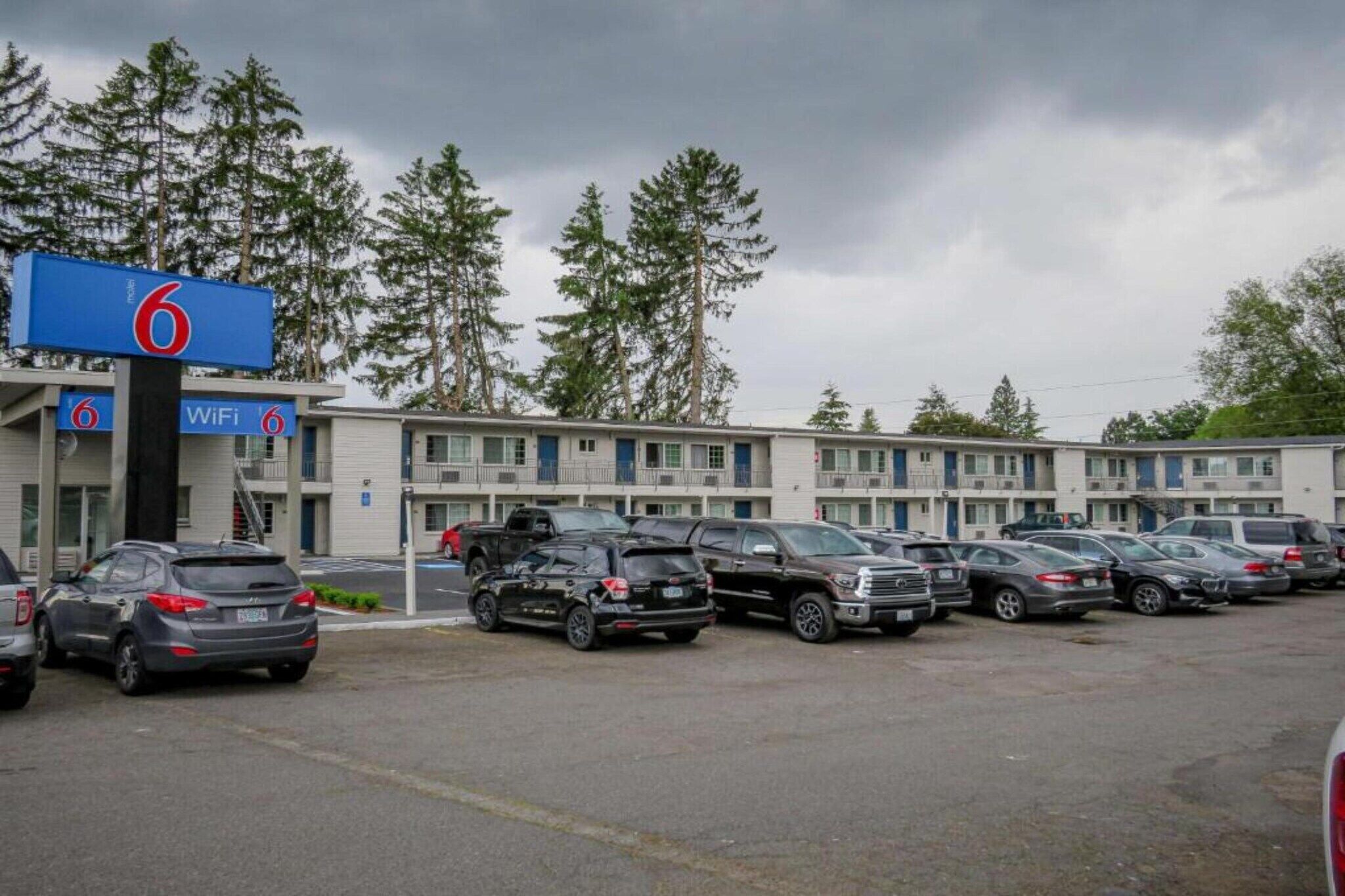 Un motel con aparcamiento, varios coches y un cartel que indica acceso a WiFi.