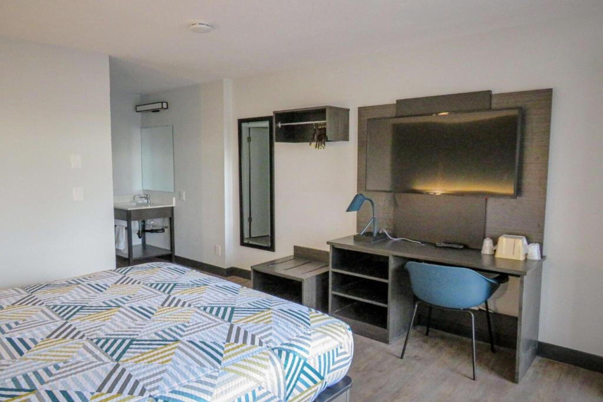 A hotel room with a bed, a desk, a chair, a mirror, and a television.