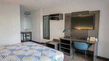 A hotel room with a bed, a desk, a chair, a mirror, and a television.