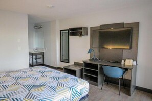 A hotel room with a bed, a desk, a chair, a mirror, and a television. - 1 Queen Bed | Non-Smoking (Tigard)