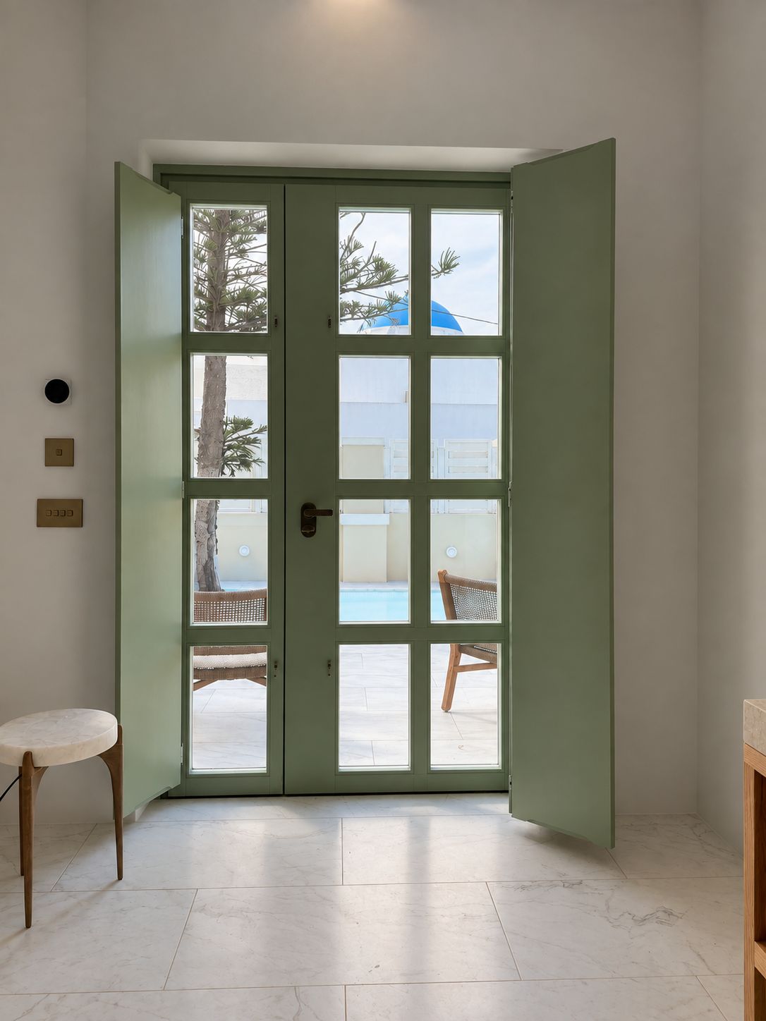A room with a green door leading to an outdoor area with a pool and chairs.