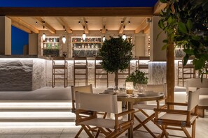 An outdoor dining area with a bar in the background, featuring a marble countertop and a variety of bottles. - Blu Suites (Imerovigli)