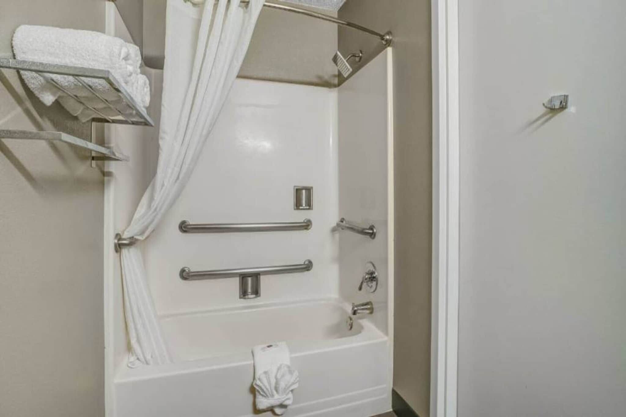 A bathroom with a bathtub, grab bars, a shower curtain, and a towel rack.