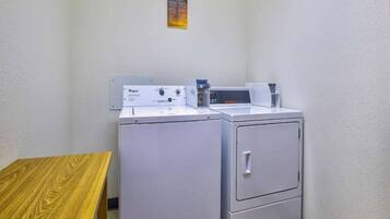 A laundry room with two white washing machines and a dryer, a wooden table, and a wall-mounted control panel.