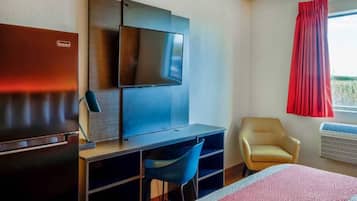 A hotel room with a bed, a desk with a chair, a television, a wardrobe, and a window with curtains.