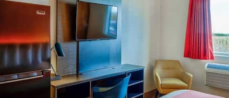 A hotel room with a bed, a desk with a chair, a television, a wardrobe, and a window with curtains.