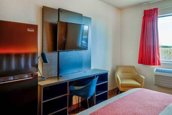 A hotel room with a bed, a desk with a chair, a television, a wardrobe, and a window with curtains.