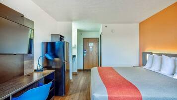 A hotel room with a bed, a desk, a chair, a refrigerator, and a television.