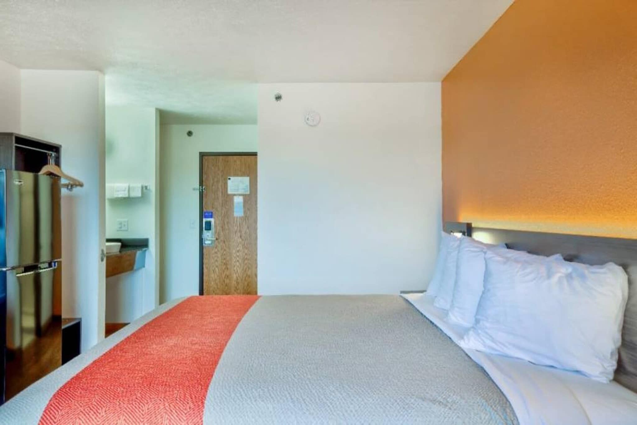 Ett hotellrum med en säng, en trädörr, ett litet kök och ett badrum.