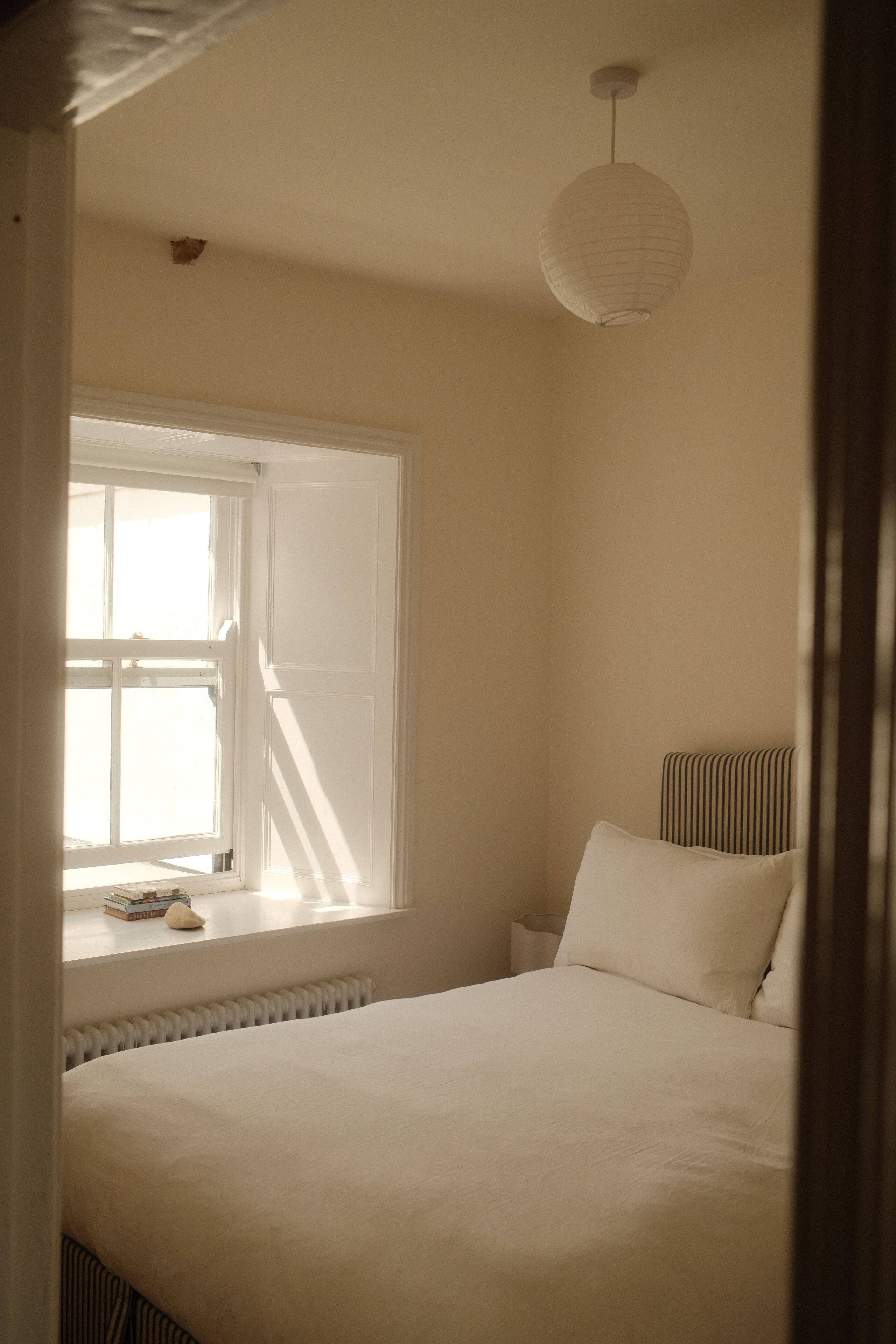 Un dormitorio con una cama grande, una ventana con persianas, un radiador y una lámpara colgante.