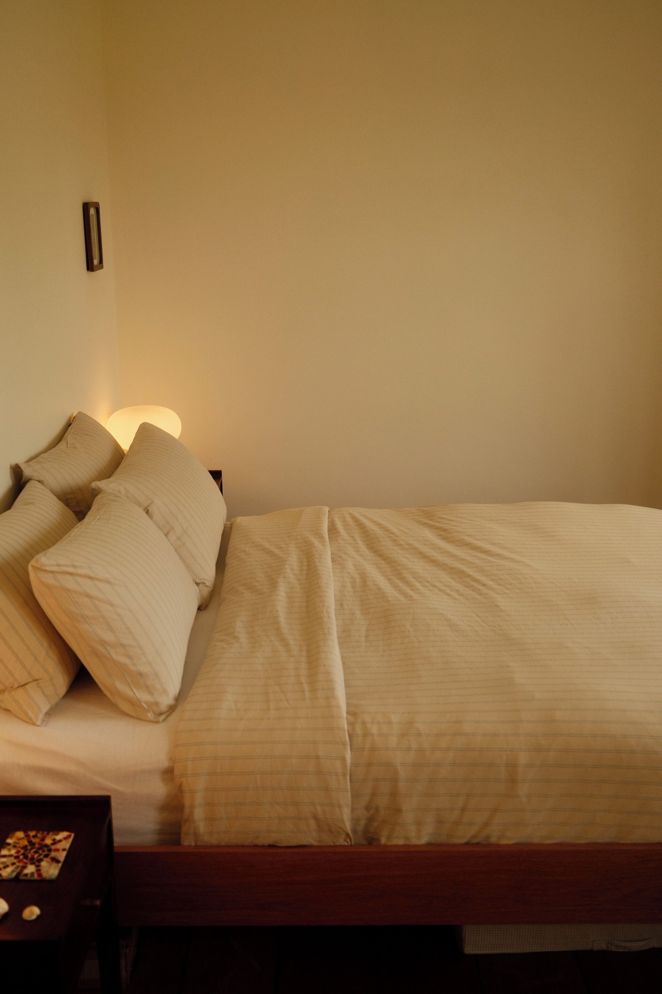 Uma cama de solteiro com estrutura de madeira, cabeceira e duas almofadas.