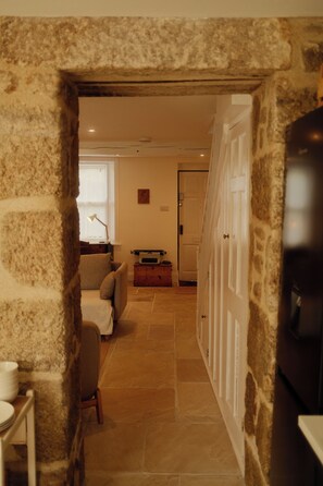 A stone-walled hallway leading to a living area with a sofa, a table, and a lamp. - Artist's Cottage in Cornwall (Penzance)
