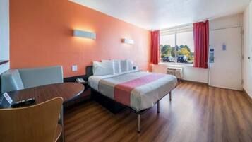 A hotel room with a bed, a desk, a chair, and a window with curtains.