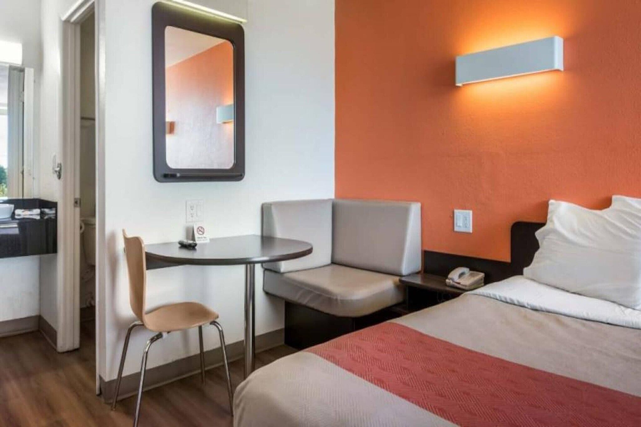 Een hotelkamer met een bed, een bureau, een stoel, een klein tafeltje, een nachtkastje en een wandlamp.