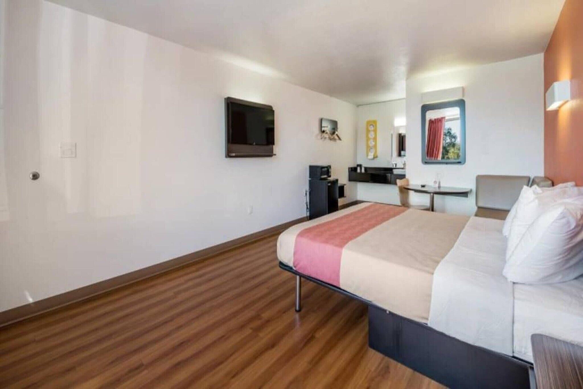 A hotel room with a bed, a desk, a chair, a television, and a kitchenette.