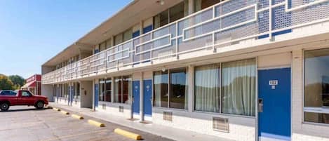 A motel with a row of rooms, a covered parking area, and a red truck parked outside.
