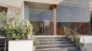 A modern building with a glass entrance, steps leading up to a wooden door, and potted plants on the steps.