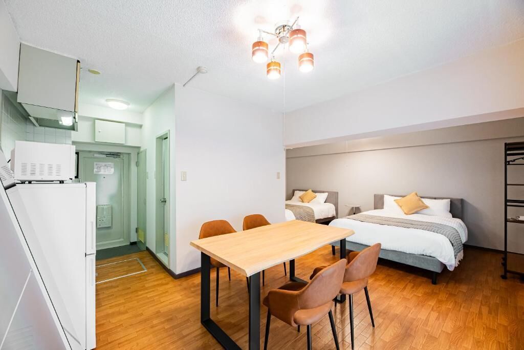 A compact room with a bed, a dining table with chairs, a kitchenette, and a ceiling light fixture.