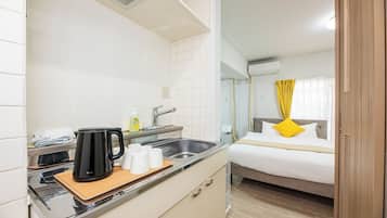 A compact hotel room with a kitchenette, a bed with a yellow pillow, and a bathroom with a shower.