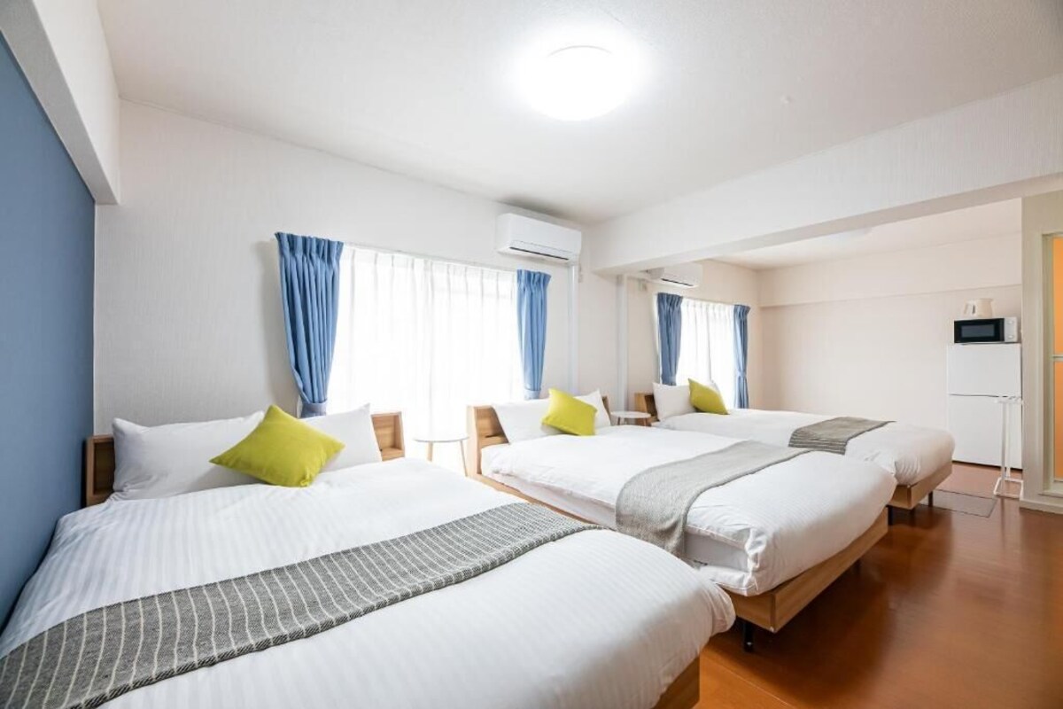 A hotel room with three beds, a microwave, and an air conditioning unit.