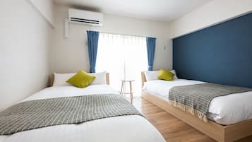 A hotel room with two beds, a small table, and an air conditioning unit.