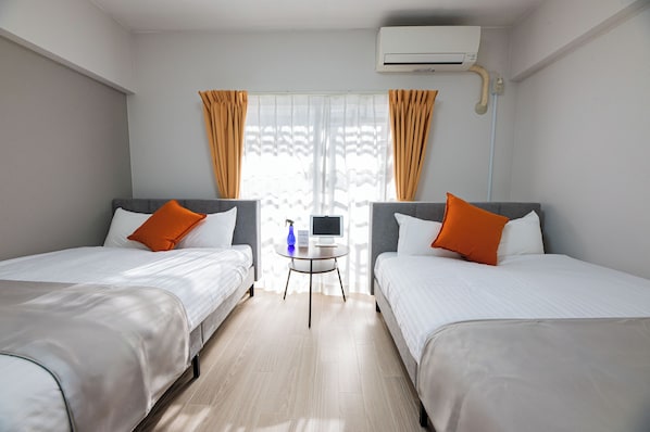A hotel room with two beds, a small table, and an air conditioning unit. - Central Heights (Fukuoka City Chuoku Watanabedori)