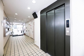 A hallway with a tiled floor, an elevator, and a door with a number display. - Central Heights (Fukuoka City Chuoku Watanabedori)