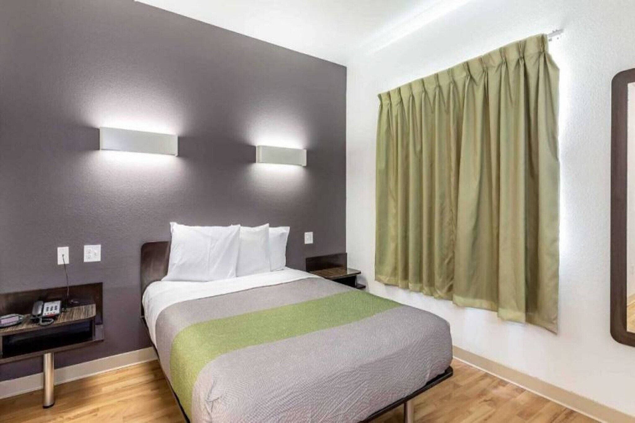 Quarto de hotel com cama, mesas de cabeceira, telefone e janela com cortinas.