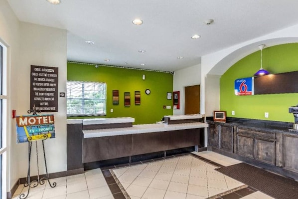 A reception area with a green wall, a counter, and a sign indicating a motel with TV and phones. - 1 Queen Bed | Non-Smoking, Kitchen (Orange)