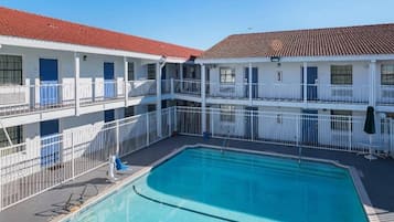 A hotel with a swimming pool, multiple balconies, and a red-tiled roof.