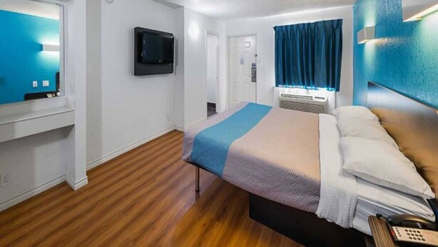 A hotel room with a bed, a TV, a desk, and a window with curtains. - 1 King Bed | Smoking (Grand Prairie)