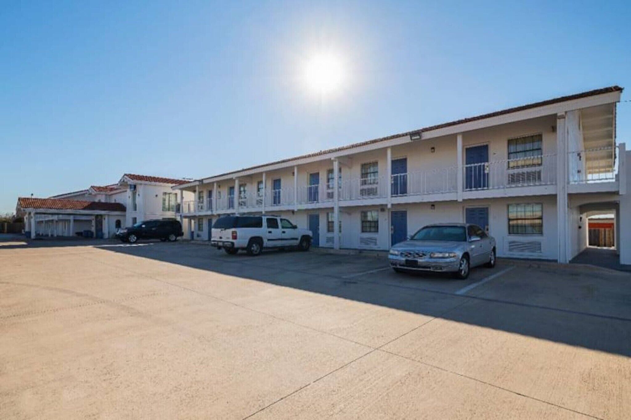A motel with multiple rooms, a parking lot, and a clear sky.