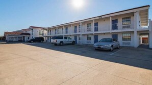 A motel with multiple rooms, a parking lot, and a clear sky. - 1 King Bed | Smoking (Grand Prairie)