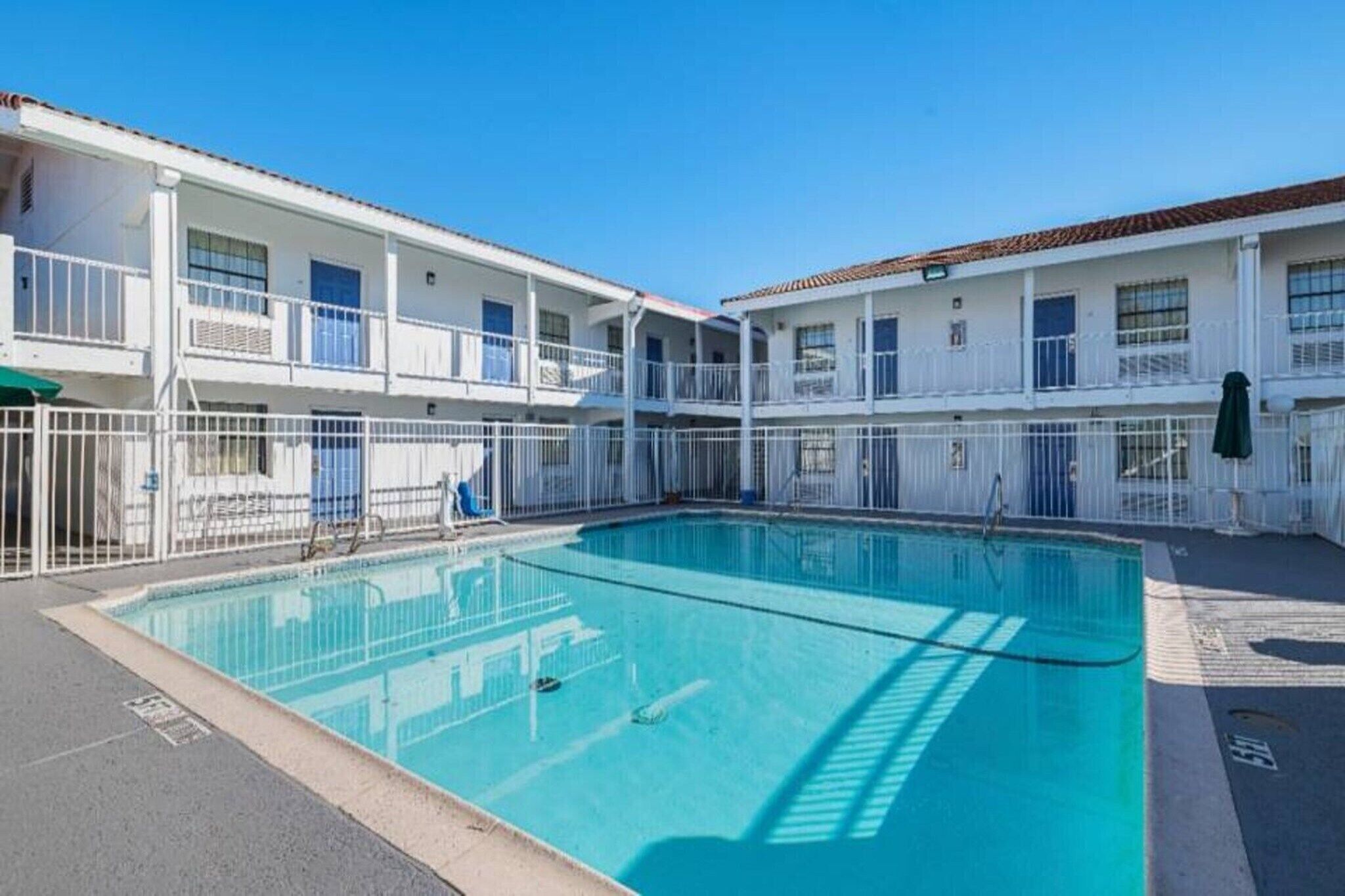 A pool area with a clear blue pool surrounded by white railings and a two-story building with balconies.