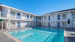 A pool area with a clear blue pool surrounded by white railings and a two-story building with balconies. - 1 King Bed | Smoking (Grand Prairie)