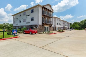 A multi-story hotel with a stone facade, a red car parked in front, and a clear sky. - 1 Queen Bed | Mobil Access Tub Nsmk Kitchen (Orange)