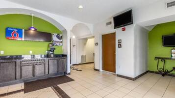 Una hall d'albergo con una reception, una macchina per il caffè, un televisore e un cartello che indica un Studio 6.