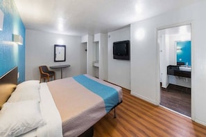 A hotel room with a bed, a desk, a chair, a television, and a bathroom. - 1 King Bed | Non-Smoking (Grand Prairie)