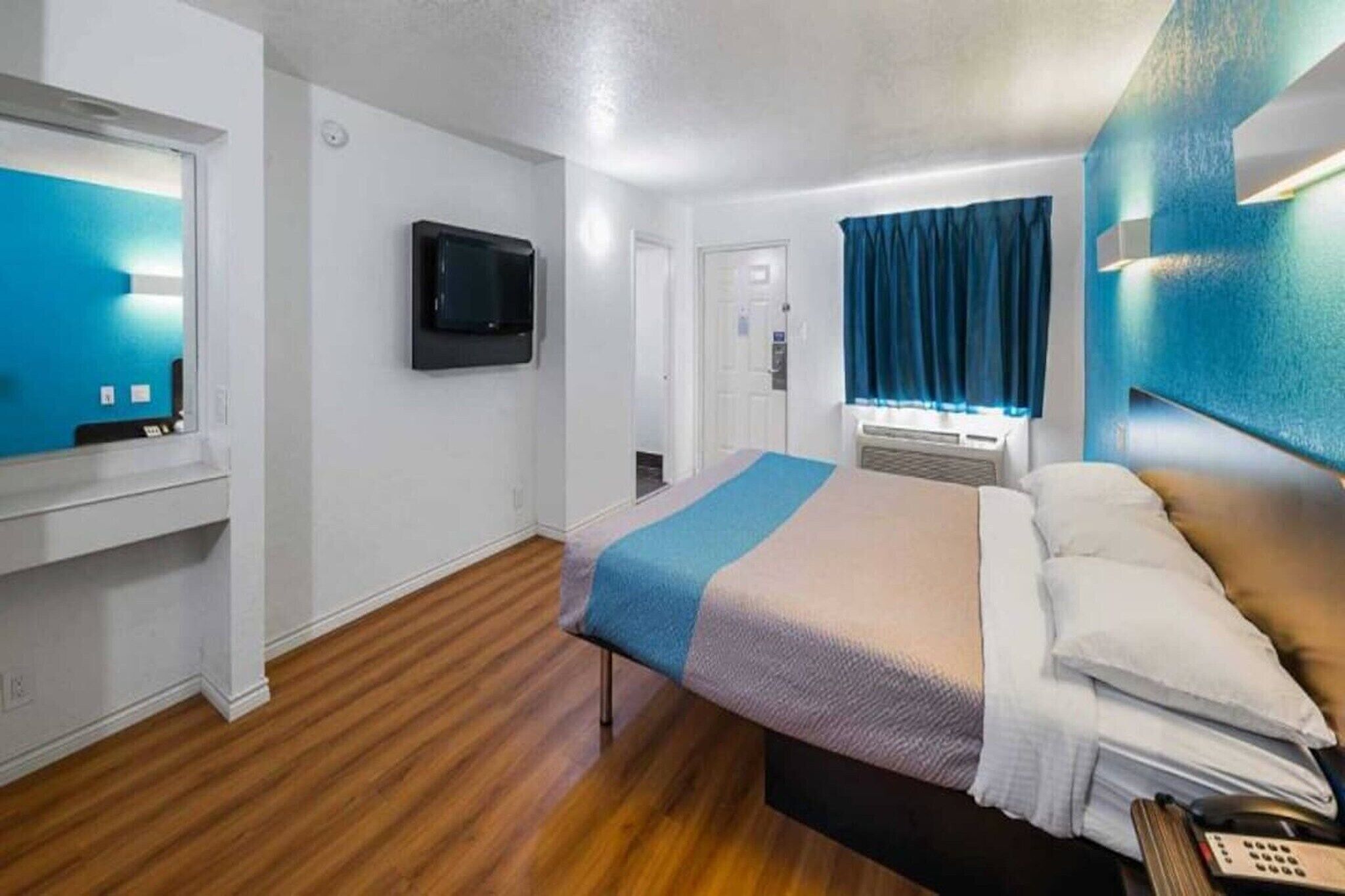 A hotel room with a bed, a TV, a desk, and a window with curtains.