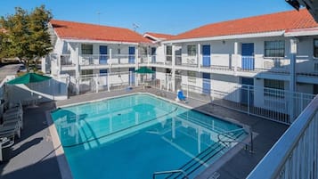 A hotel with a central swimming pool, multiple balconies, and a red-tiled roof.