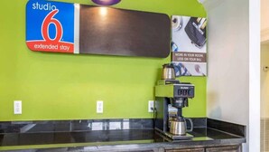 Une petite cuisine équipée d’une machine à café, une enseigne indiquant « studio 6, séjour prolongé », et un luminaire fixé au mur.