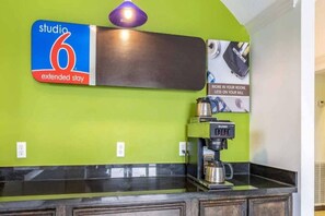 A kitchenette with a coffee machine, a sign for 'studio 6 extended stay', and a wall-mounted light fixture. - 2 Full Beds | Suite, Non-Smoking, Kitchen (Orange)