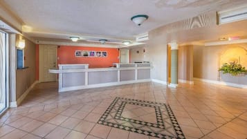 A spacious lobby with a reception desk, a patterned floor design, and a large plant.