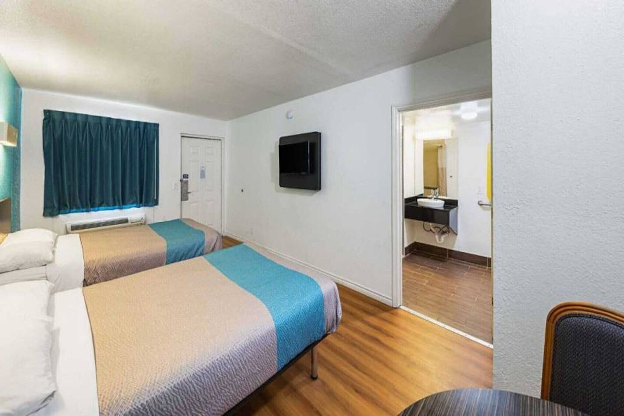 Habitación de hotel con dos camas, un televisor, una puerta y un baño visible a través de una puerta abierta.