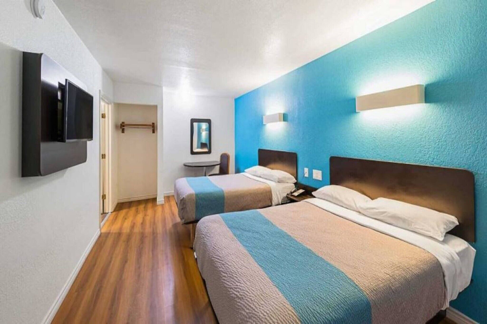 Habitación de hotel con dos camas, un televisor de pantalla plana, una mesita y un espejo.