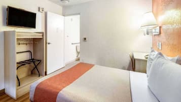 Ein Hotelzimmer mit einem Bett, einem an der Wand befestigten Fernseher, einem Kleiderschrank und einem Schreibtisch mit Lampe.