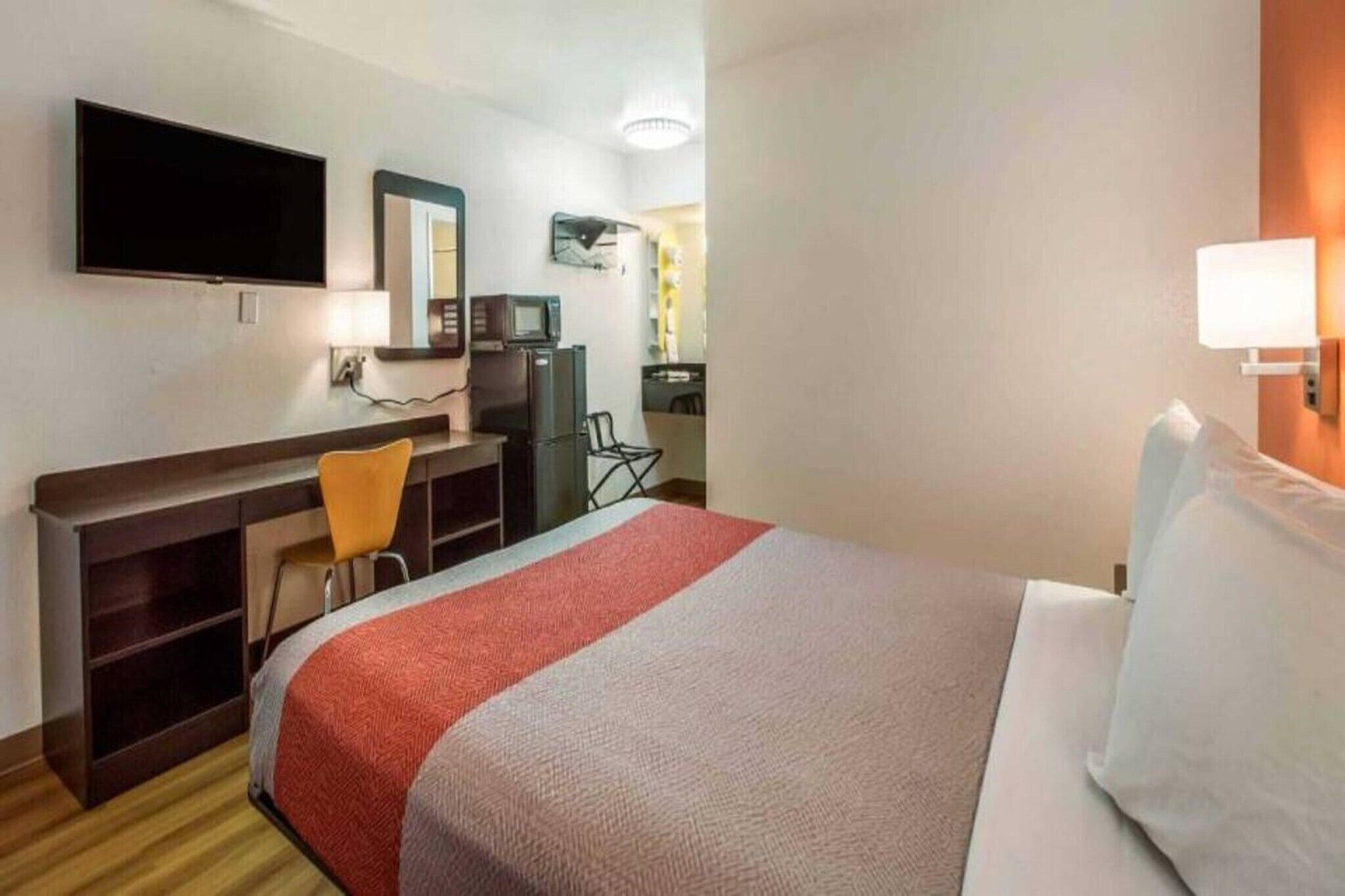 Una habitación de hotel con cama, escritorio, silla, televisión y espejo.