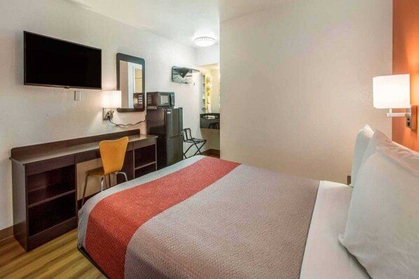 A hotel room with a bed, a desk, a chair, a television, and a mirror.