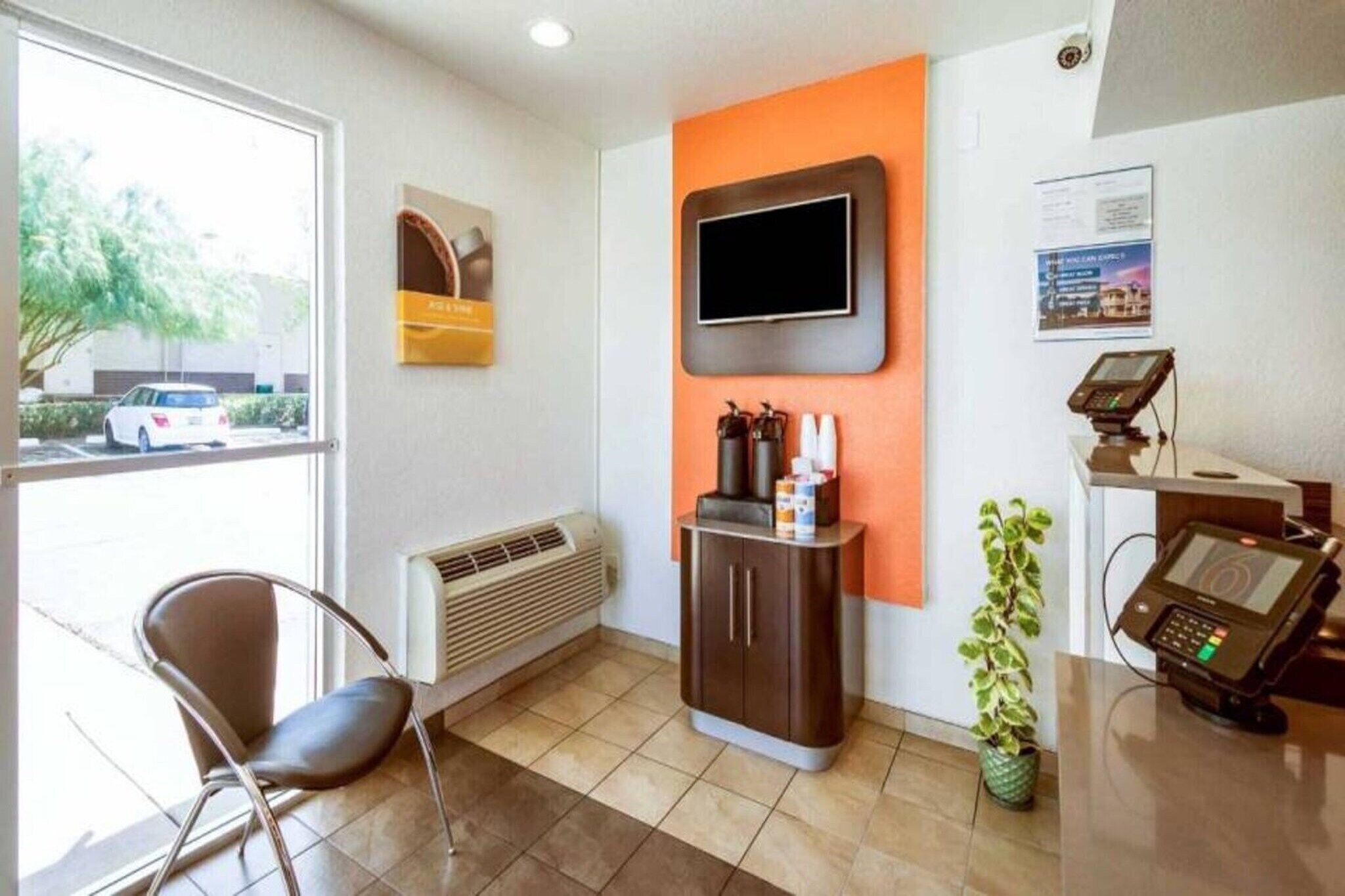 A reception area with a chair, a TV mounted on the wall, a vending machine, and a plant.