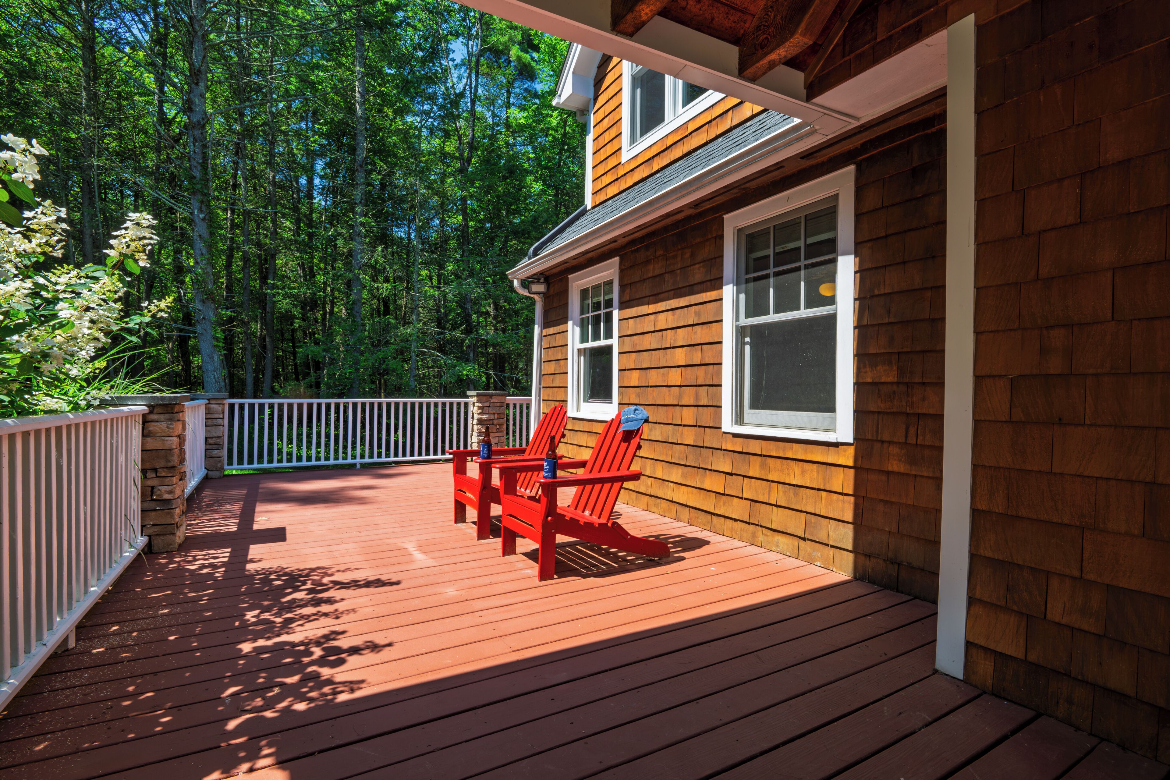 A wooden deck with two red Adirondack chairs and a stone pillar.